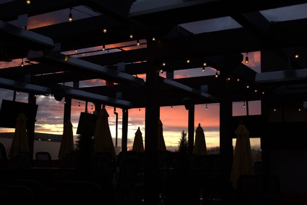 patio with umbrellas and gazebo with lighting hung from it in front of a sunset